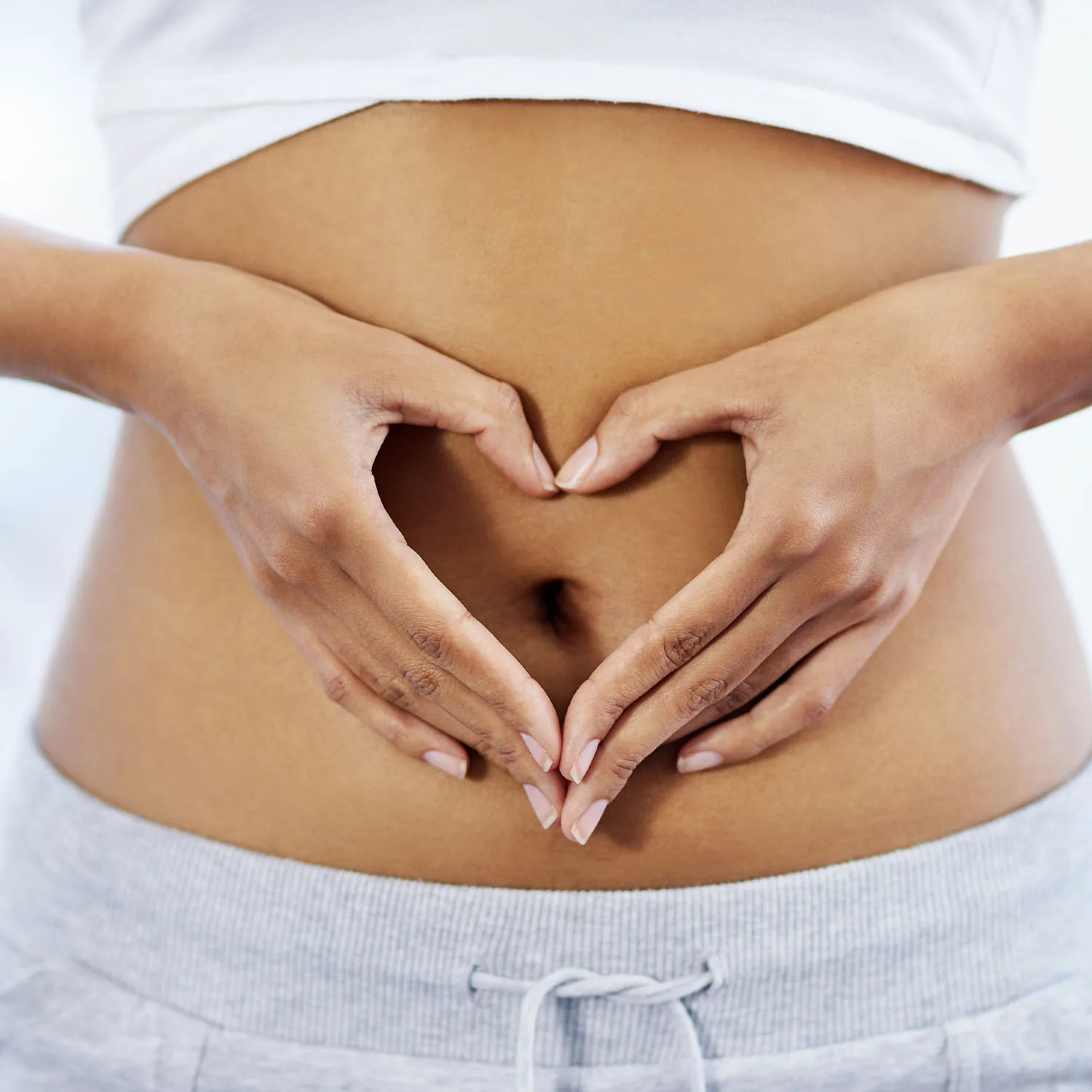 Eine Nahaufnahme eines Bauchs zeigt zwei Hände, die ein Herz um den Bauchnabel formen.
