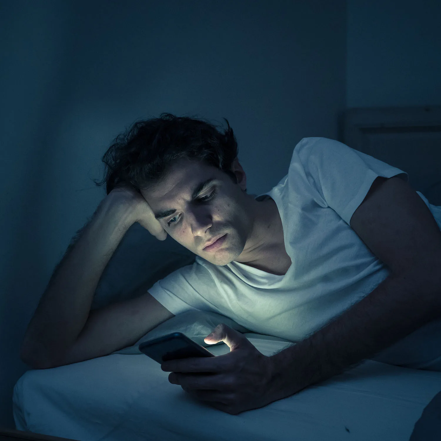 Ein Mann liegt in einem dunklen Zimmer und schaut auf sein Handy.