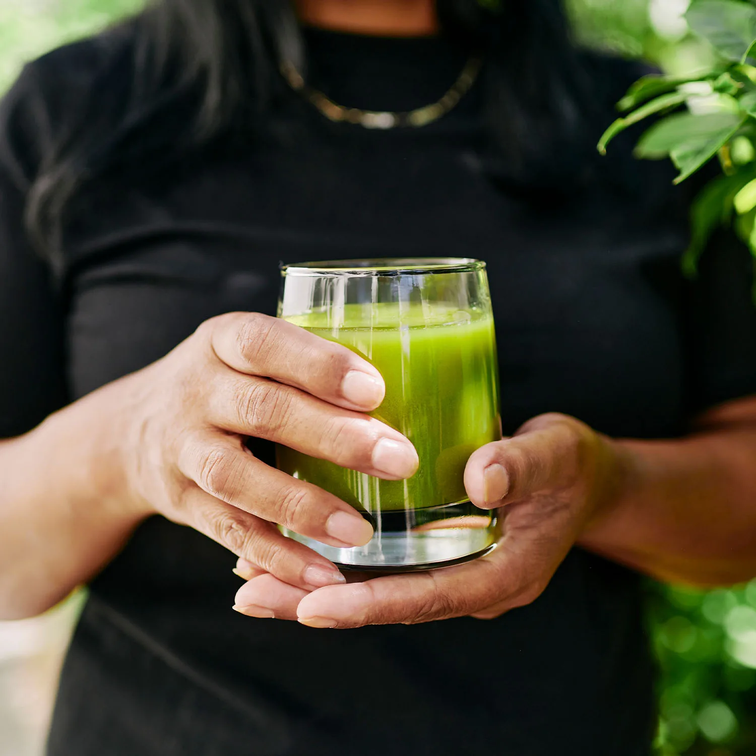 Die Nahaufnahme zeigt eine Person die ein Glas mit einem grünen Smoothie in die Kamera hält.